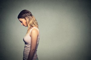 Sad lonely young woman looking down isolated on gray wall background